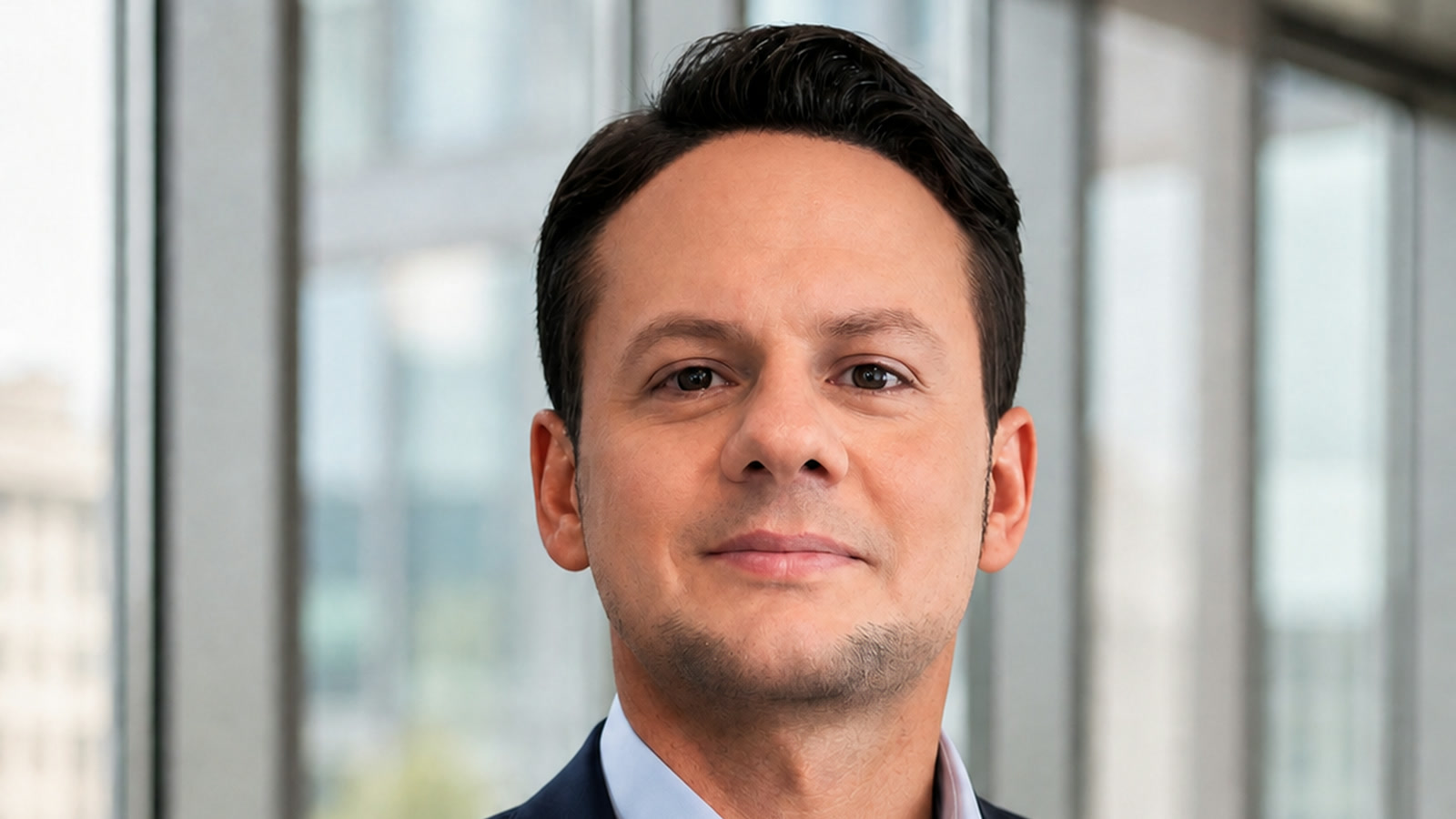 Jared Mastroianni wearing a navy blazer and light blue shirt in a contemporary office setting.